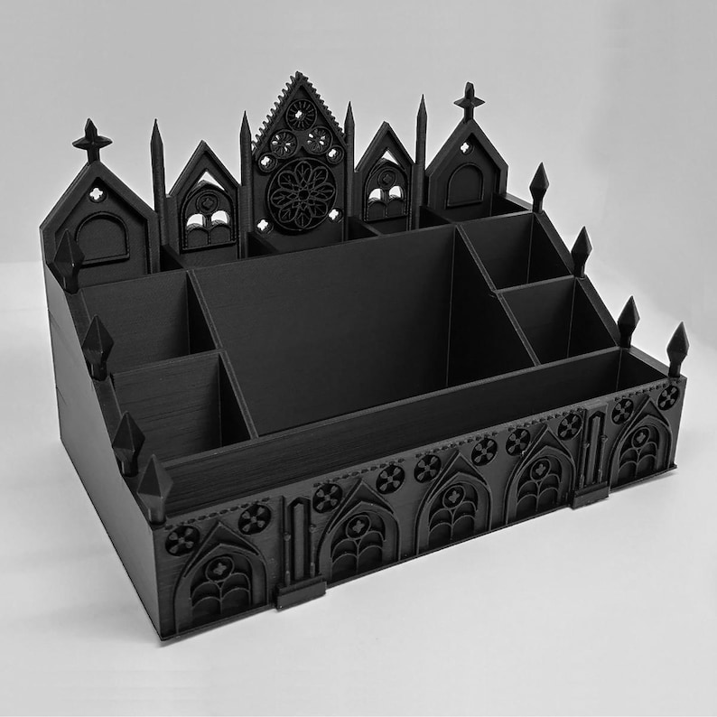 May include: Black desk organizer with a gothic cathedral design. The organizer features multiple compartments and a decorative facade with arched windows, crosses, and a rose window. The overall design is symmetrical and detailed.