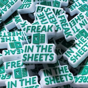 May include: A pile of white and green silicone charms with the text "Freak in the Sheets" and an Excel logo.