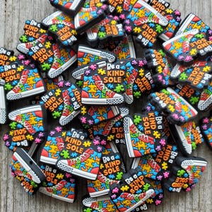 May include: A close-up of a group of colorful shoe charms with a puzzle piece design and the text "Be a Kind Sole".