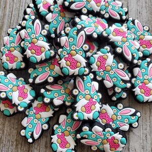 May include: A group of colorful Easter gnome charms with bunny ears and a floral pattern. The gnomes are wearing pink and white hats and have white beards. The charms are made of a soft, flexible material and are perfect for adding a touch of whimsy to your Easter decorations.