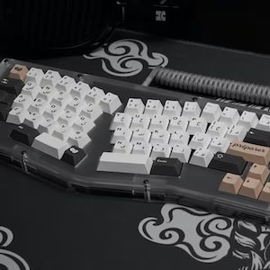 Peut inclure: Un clavier mécanique blanc et noir avec un boîtier en plastique transparent. Le clavier possède un jeu de touches personnalisées avec une variété de couleurs et de motifs. Le clavier est sur un tapis de souris noir avec un motif nuage.