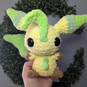 Może przedstawiać: Pluszowa zabawka postaci Pokemon w kolorze ż&oacute;łtym i zielonym, wykonana na szydełku. Zabawka ma duże czarne oczy i zielony r&oacute;g.