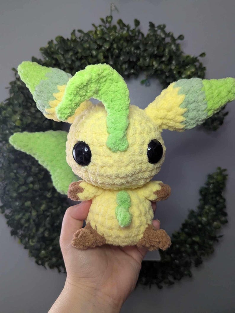 Może przedstawiać: Pluszowa zabawka postaci Pokemon w kolorze ż&oacute;łtym i zielonym, wykonana na szydełku. Zabawka ma duże czarne oczy i zielony r&oacute;g.