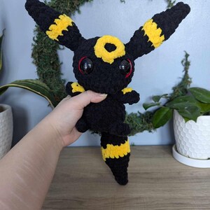 Może przedstawiać: Pluszowa zabawka w kolorze czarnym i ż&oacute;łtym, przypominająca postać z Pokemon&oacute;w z dużymi oczami.