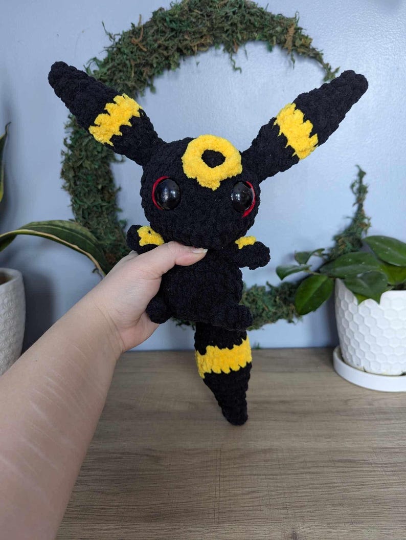 Może przedstawiać: Pluszowa zabawka w kolorze czarnym i ż&oacute;łtym, przypominająca postać z Pokemon&oacute;w z dużymi oczami.