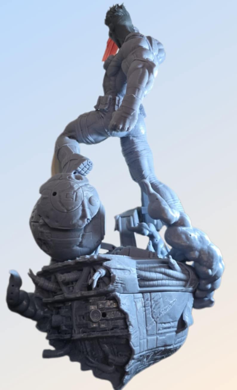 May include: A gray figurine of a muscular figure in a dynamic pose, stepping onto a detailed, futuristic base. The figure has a red accent and is surrounded by mechanical and organic elements.
