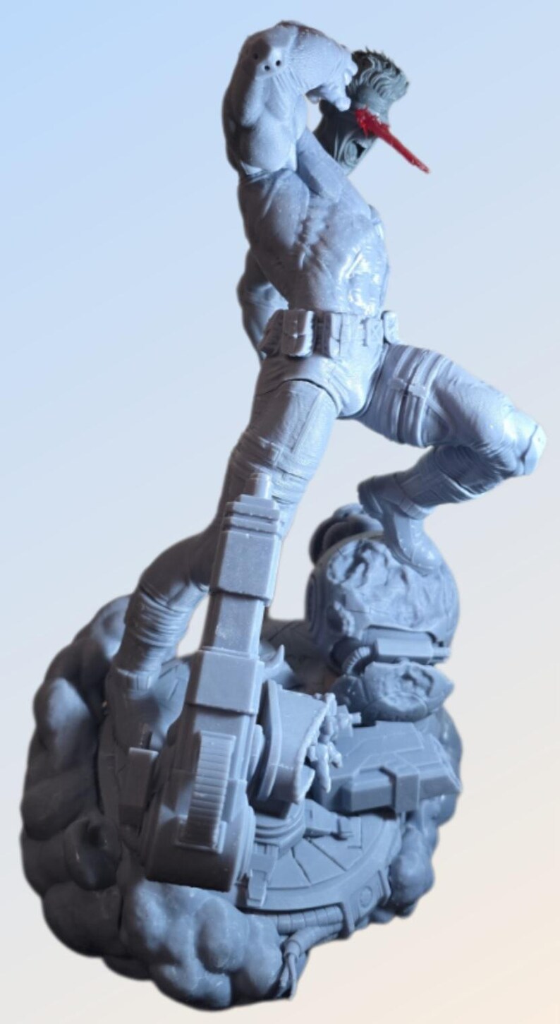 May include: A gray action figure of a muscular character in a dynamic pose, with one leg raised and arm overhead. The figure is atop a detailed base with mechanical elements. The figure has a red element on its face.
