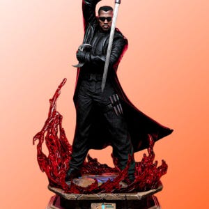 May include: A detailed figurine of a character in a black outfit, sunglasses, and a long coat, holding a sword. The figure stands on a base with red, flame-like accents. The base has an inscription in a foreign language.