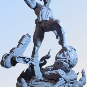 May include: A gray figurine of a muscular character in a dynamic pose, with one arm raised and a red visor over one eye. The figure stands on a detailed base with mechanical elements and a cloud-like effect, suggesting action and power.
