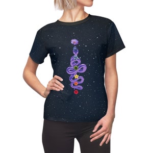 May include: A black t-shirt with a white speckled pattern. The shirt features a purple snake design adorned with colorful flowers. The snake is vertically oriented, creating a unique and eye-catching graphic on the front of the tee.