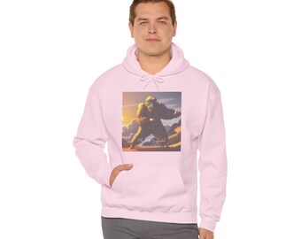 Puede incluir: Sudadera con capucha rosa claro con un bolsillo delantero y un gráfico de una criatura grande y peluda en una escena de puesta de sol. El gráfico incluye el texto "The Lost Bigfoot" y "Adventure Awaits". La sudadera con capucha la lleva una persona.