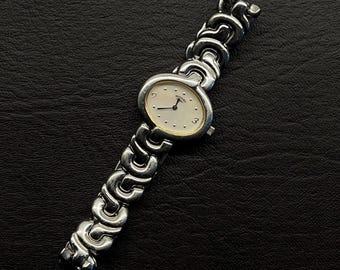 Reloj de cuarzo giratorio vintage para mujer con pulsera plateada y esfera blanca.
