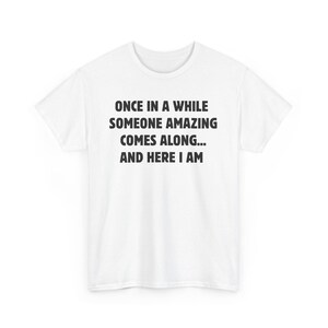 Op de afbeelding: Een wit t-shirt met de zwarte tekst: "ONCE IN A WHILE SOMEONE AMAZING COMES ALONG... AND HERE I AM". Het t-shirt heeft korte mouwen en is gemaakt van een zachte stof.