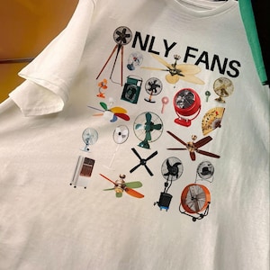 May include: White t-shirt with a graphic print of various fans and the text "ONLY FANS" in black.