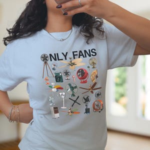 May include: A light blue t-shirt with the text "ONLY FANS" printed in black. The shirt features a design of various types of fans, including ceiling fans, box fans, and stand fans.