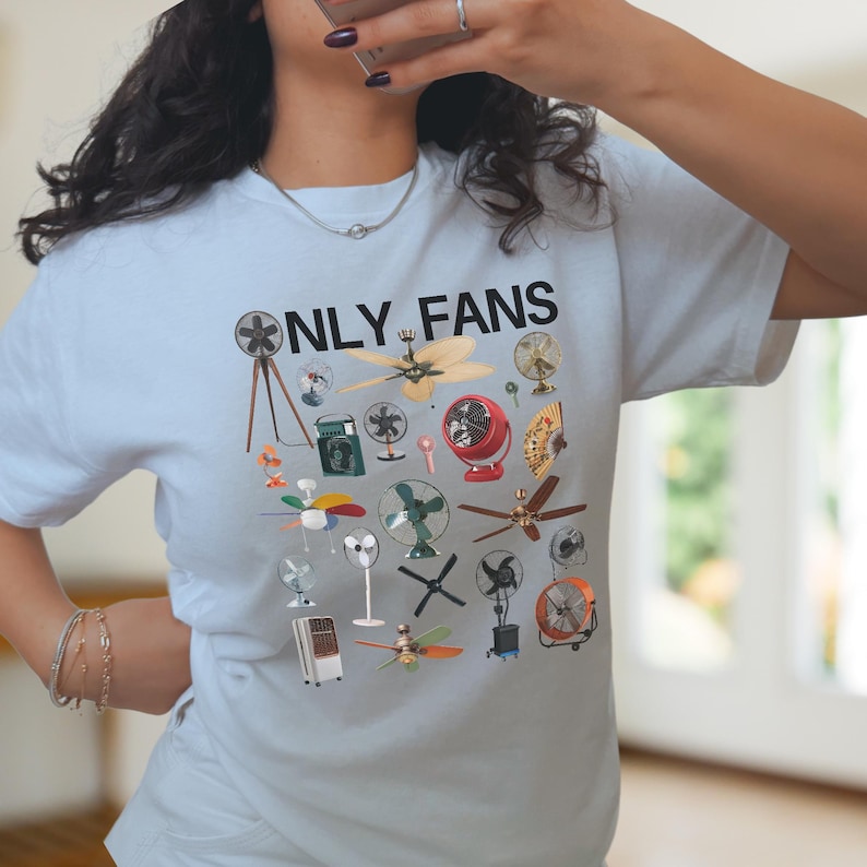 May include: A light blue t-shirt with the text "ONLY FANS" printed in black. The shirt features a design of various types of fans, including ceiling fans, box fans, and stand fans.