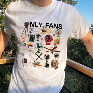 May include: White t-shirt with the text "ONLY FANS" printed in black. The shirt features a design of various types of fans, including ceiling fans, box fans, and stand fans.