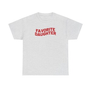 Puede incluir: Camiseta gris claro con la frase "FAVORITE DAUGHTER" en rojo en el pecho. La camiseta tiene cuello redondo y mangas cortas, adecuada para uso casual.