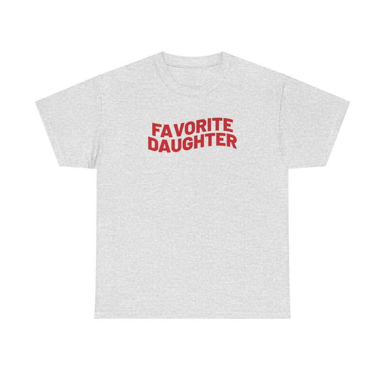 Puede incluir: Camiseta gris claro con la frase "FAVORITE DAUGHTER" en rojo en el pecho. La camiseta tiene cuello redondo y mangas cortas, adecuada para uso casual.