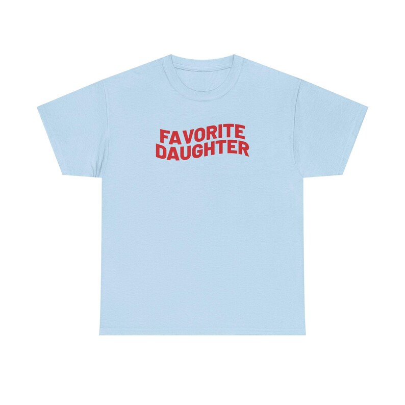 Puede incluir: Camiseta azul claro con la frase "FAVORITE DAUGHTER" en rojo en el pecho. El texto est&aacute; en una fuente audaz y juguetona. Es una prenda casual para el d&iacute;a a d&iacute;a.