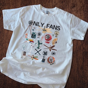 May include: White t-shirt with a graphic print of various fans and the text "ONLY FANS" in black.