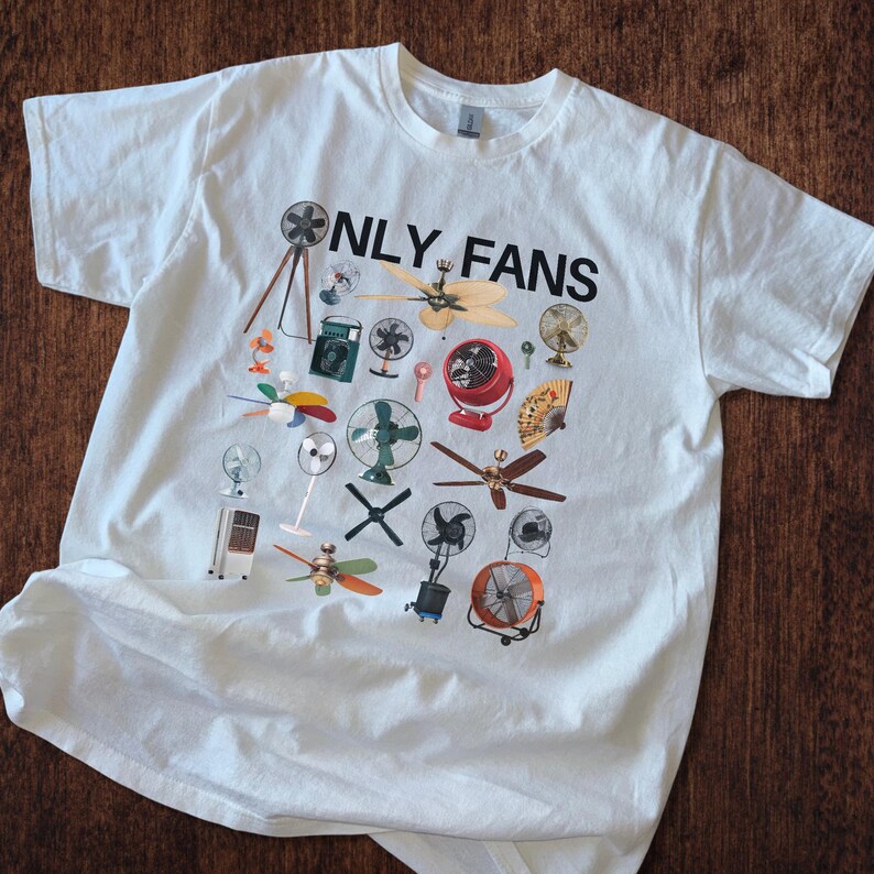 May include: White t-shirt with a graphic print of various fans and the text "ONLY FANS" in black.