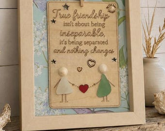 May include: A light-colored wooden frame containing a rectangular plaque with the text: True friendship isn't about being inseparable, it's being separated and nothing changes. Two figures made of sea glass and wooden beads hold a red heart.