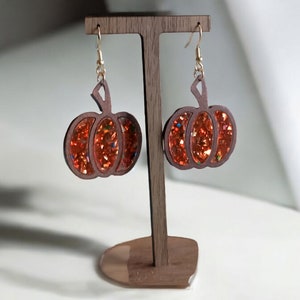May include: A pair of pumpkin-shaped earrings with gold hooks. The pumpkins are made of wood and have a glittery orange finish.