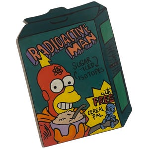 以下が含まれることがあります： 手描きの木製 Radioactive Man シリアルボックスアート。緑色の箱には、オレンジと紫色の文字で「Radioactive Man」と書かれています。キャラクターは、横に「Cereal Pal」が描かれたシリアルを食べています。