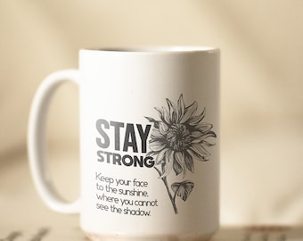 May include: White ceramic mug with a black and white sunflower graphic and the text "STAY STRONG Keep your face to the sunshine. where you cannot see the shadow."