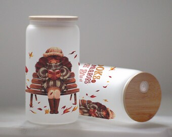 May include: Two white frosted glass jars with bamboo lids. The jars have illustrations of a girl reading a book on a bench with autumn leaves. The text on the jar reads "Books & Mirrors & Sun".