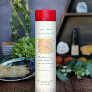 May include: Red candle with the words "Seduction" and "Reiki Energy Charged Candle" on the label. The label also includes the text "May all loving emotions contained within me flow freely to the surface, inspiring pleasure and attracting love. I am a child of love." and "ESSENTIAL OIL FRAGRANCE BLEND cedar, musk, pine patchouli and juniper". The candle is labeled "Crystal Journey Candles" and "Handcrafted in the USA Herbal Magic Candles".