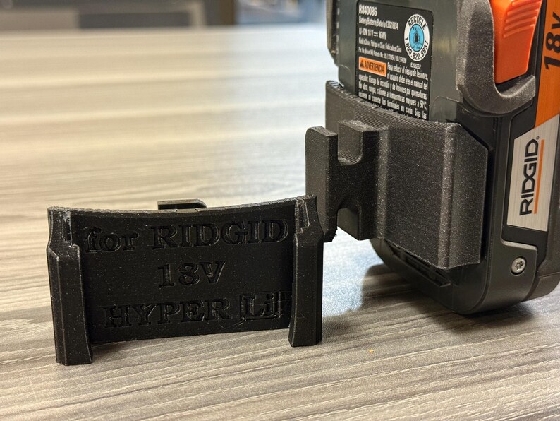 Puede incluir: Soporte de bater&iacute;a negro impreso en 3D para bater&iacute;as Ridgid 18V Hyper Lithium. El soporte est&aacute; dise&ntilde;ado para sujetar la bater&iacute;a de forma segura. El texto "For RIDGID 18V HYPER Li" est&aacute; impreso en el soporte.