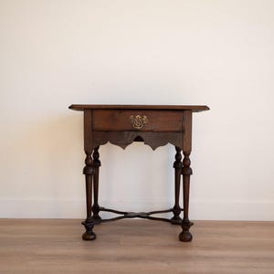 May include: A dark brown antique side table with a single drawer and ornate brass hardware. The table has carved legs and a decorative apron. The table is approximately 28 inches tall.