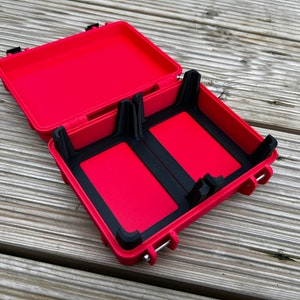 May include: Red hard plastic case with black rubber inserts for holding two items. The case is open and the lid is propped up.