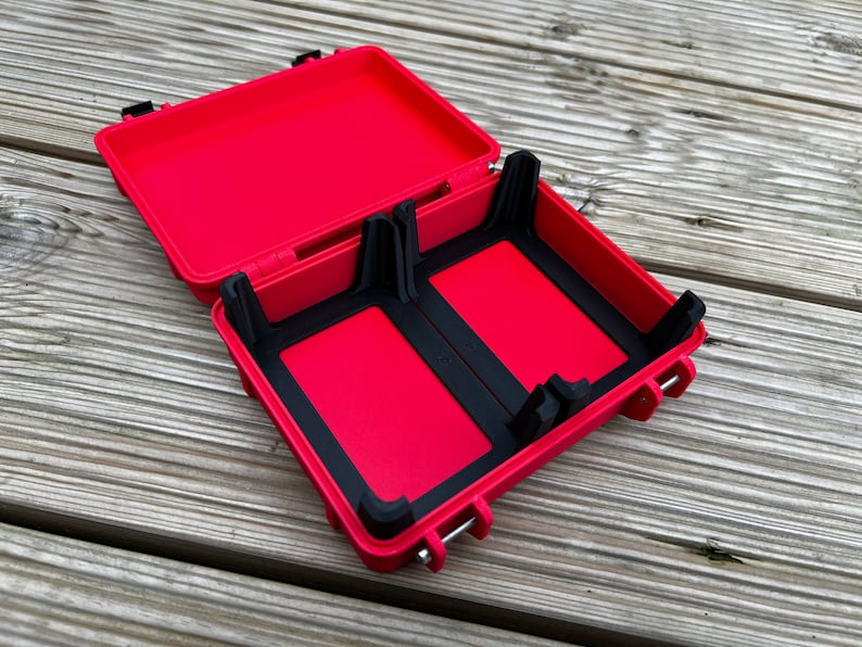 May include: Red hard plastic case with black rubber inserts for holding two items. The case is open and the lid is propped up.