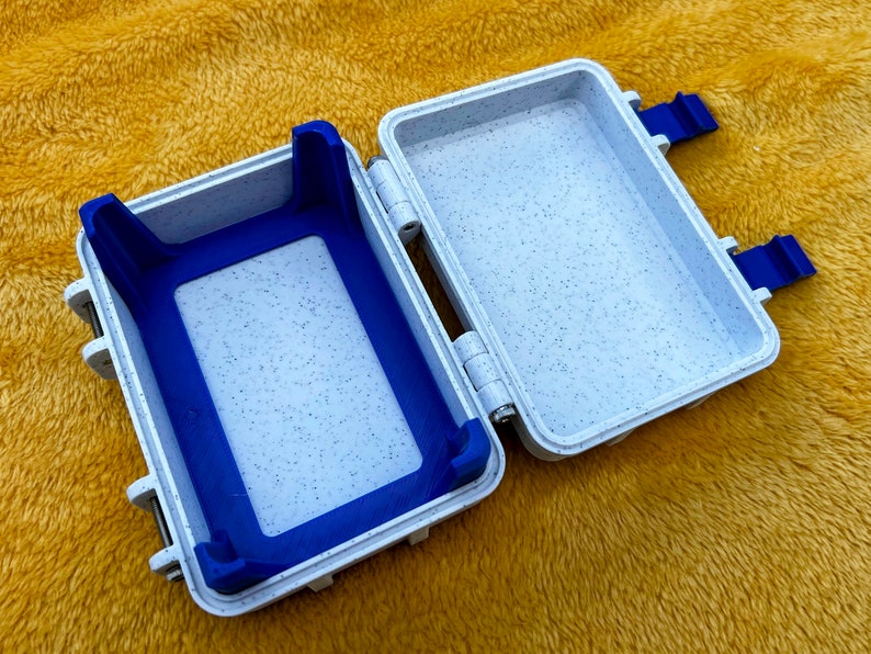 Op de afbeelding: Een witte plastic opbergdoos met een blauwe rubberen inzet. De doos heeft twee sluitingen en een scharnier.