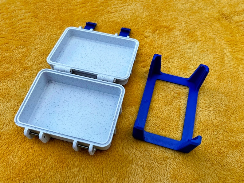 Op de afbeelding: Een witte plastic opbergdoos met een blauwe sluiting en een blauwe plastic standaard. De doos is open en de standaard is apart.