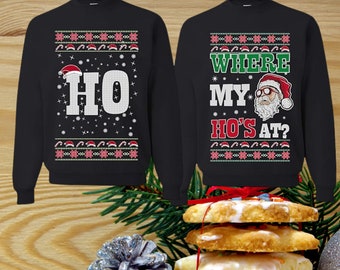 May include: Two black Christmas sweaters with a festive design. One sweater says "HO" with a Santa hat. The other sweater says "WHERE MY HO'S AT?" with a Santa wearing sunglasses.
