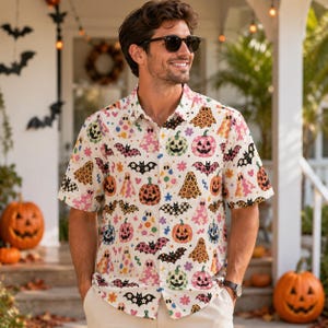 May include: A short-sleeved button-down shirt featuring an all-over print of colorful Halloween motifs including ghosts, jack-o'-lanterns, and bats in shades of pink, orange, yellow, and black on a cream-colored background with a classic collar.