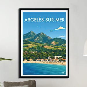 Könnte beinhalten: Ein gerahmtes Reiseplakat für Argeles-sur-Mer mit einer Küstenlandschaft. Das Plakat zeigt den Namen der Stadt in weißen Buchstaben vor blauem Himmel. Das Kunstwerk zeigt grüne Berge, ein blaues Meer und einen Strand mit Gebäuden.