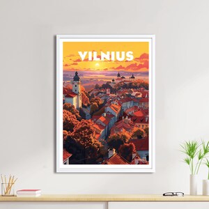 Puede incluir: Una ilustración colorida de la ciudad de Vilnius, Lituania, con el texto "VILNIUS" en letras blancas en la parte superior de la imagen. La ilustración representa un paisaje urbano con edificios de techos rojos, un campanario de iglesia y árboles en primer plano. El cielo es de un naranja y amarillo vibrantes, lo que sugiere una puesta de sol.