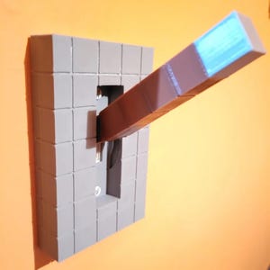 May include: A grey, cube-patterned light switch cover with a brown and blue lever extending outwards. The switch is mounted on an orange wall, creating a striking contrast.