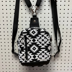 May include: Black and white geometric patterned crossbody bag with adjustable straps. The bag has a zipper closure and the text "Over the Moon" is printed on the front.