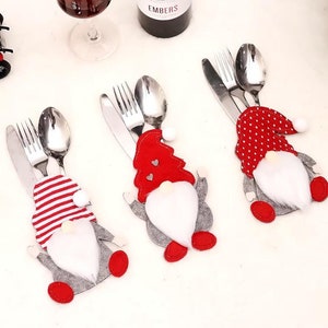 May include: Christmas-themed silverware holders shaped like gnomes. Each gnome has a red hat, white beard, and gray body. One has red and white striped clothing, another has a red tree, and the third has red polka dots. Silverware is visible.