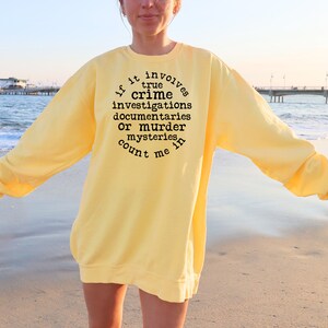 May include: A yellow sweatshirt with black text that reads "If it involves true crime investigations, documentaries, or murder mysteries, count me in."