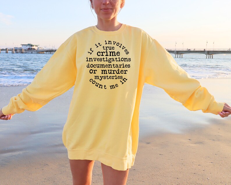 May include: A yellow sweatshirt with black text that reads "If it involves true crime investigations, documentaries, or murder mysteries, count me in."