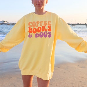 May include: A yellow sweatshirt with the text "COFFEE BOOKS & DOGS" in a retro font with orange, pink, and purple colors.