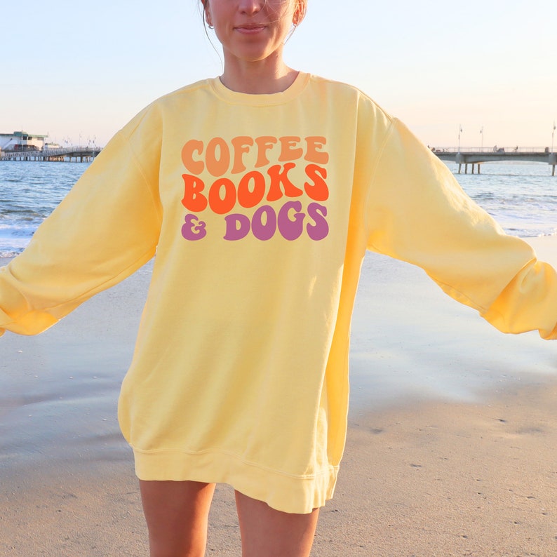 May include: A yellow sweatshirt with the text "COFFEE BOOKS & DOGS" in a retro font with orange, pink, and purple colors.