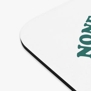 Op de afbeelding: Een witte muismat met een zwarte rand. De tekst "NOW" is in teal groen op de muismat gedrukt.